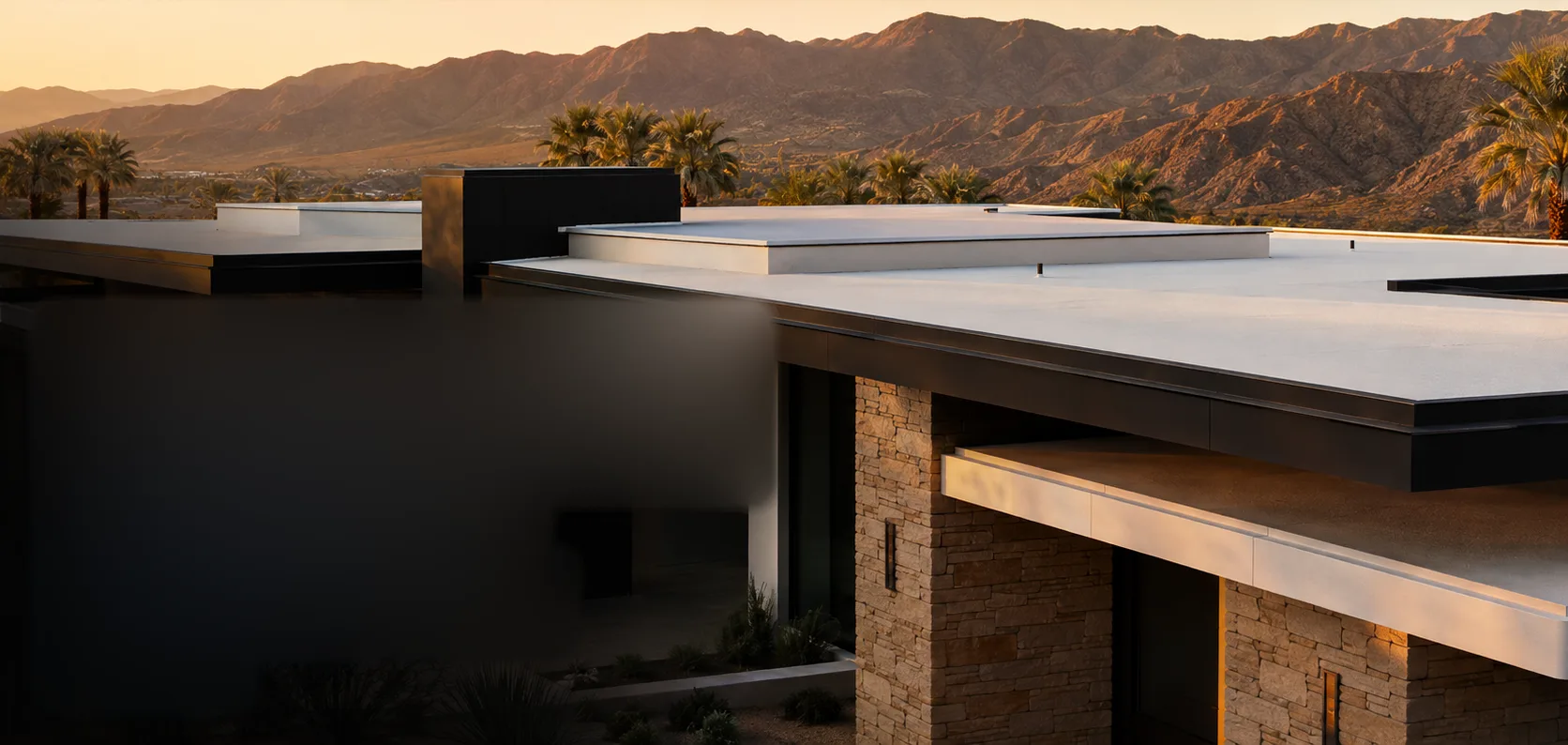 A low desert-modern residence at golden hour, its white SPF roof deck and deep dark eaves set against the Coachella Valley mountains