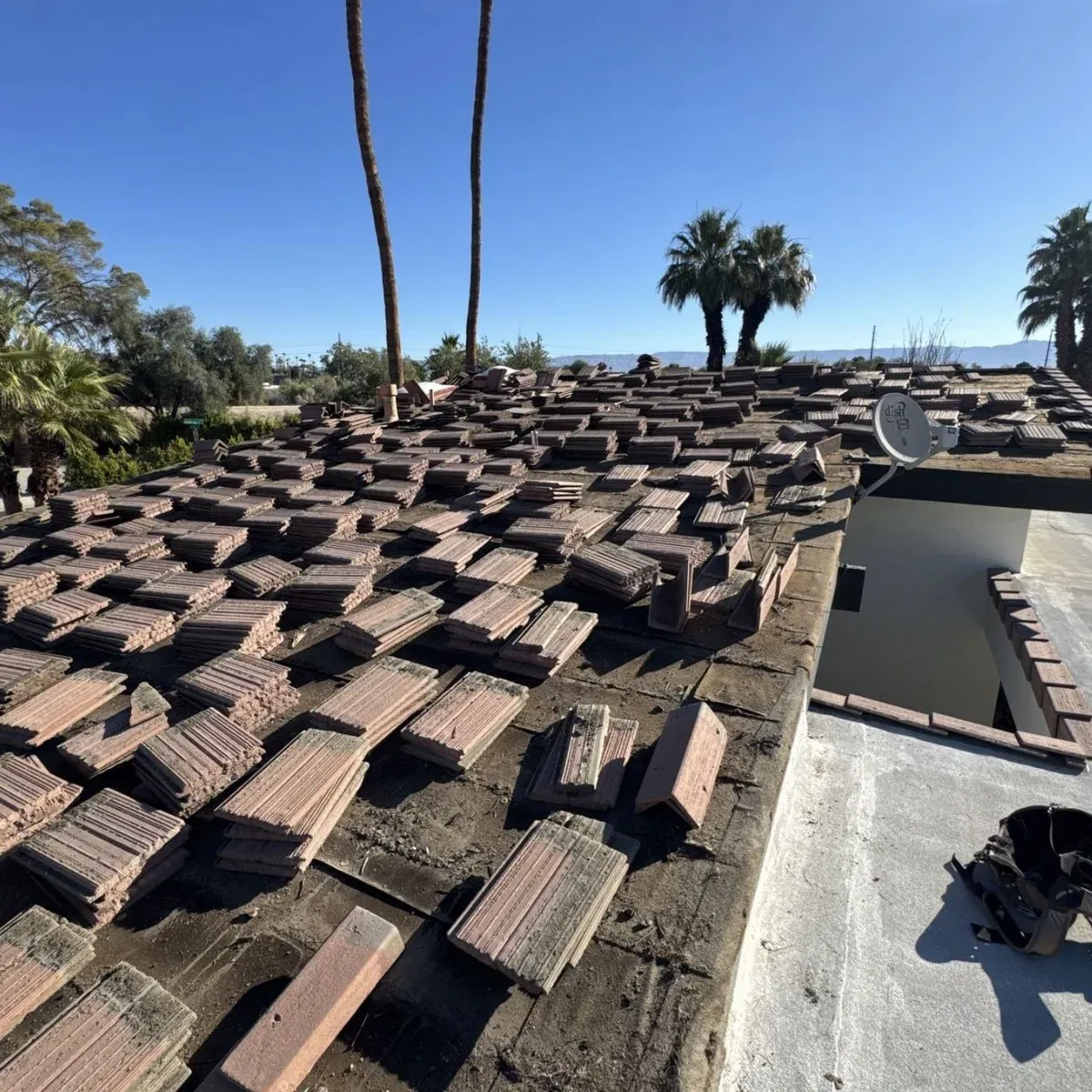 Roof tiles lifted and stacked in rows across a roof while the underlayment beneath is replaced