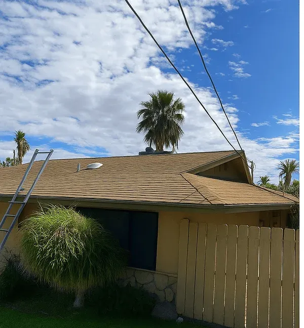A single-storey home before reroofing: worn brown shingles, a ladder resting against the eave and a tan wooden fence
